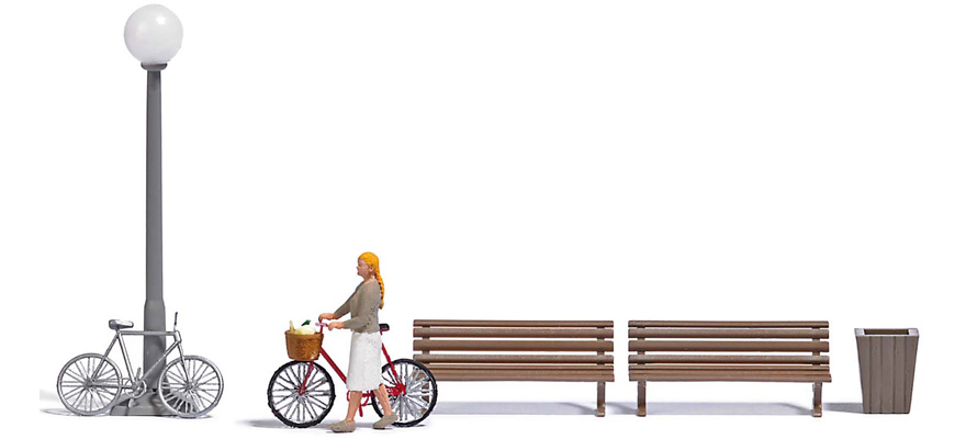 Dame poussant son vélo avec panier rempli de légumes‚ 2 bancs‚ 1 lampadaire‚ 1 poubelle et un 2ième vélo