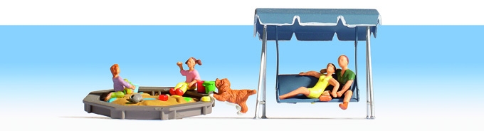 2 Enfants et un chien jouent dans un bac  sable les parents se reposent sur une balancelle